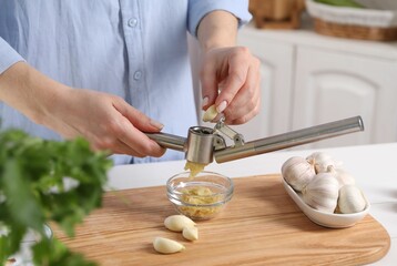 Woman squeezing garlic with press at wooden table in kitchen, closeup