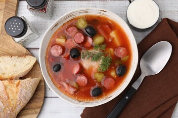Meat solyanka soup with thin dry smoked sausages served on white wooden table, flat lay