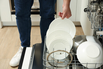 Man loading dishwasher with plates indoors, closeup