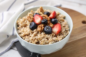 Tasty oatmeal with strawberries, blueberries and walnuts in bowl on white wooden table, closeup