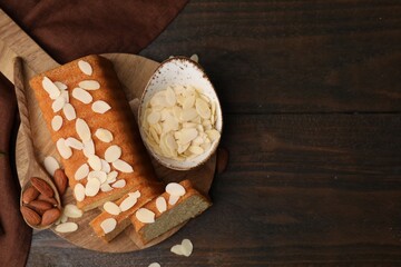 Cake with fresh almond flakes, spoon and nuts on wooden table, top view. Space for text