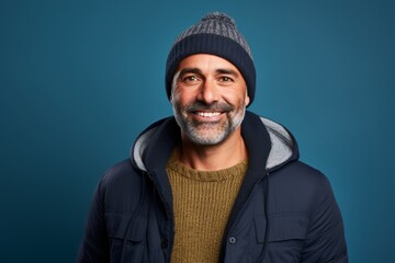 Portrait of a smiling man in his 50s dressed in a warm ski hat while standing against solid color...