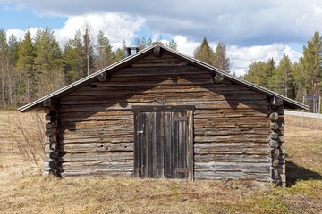 Old weatherd log building in spring with clouds in the sky, Lapland, Finland.