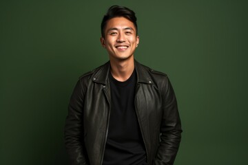 Naklejka premium Portrait of a smiling asian man in his 20s sporting a classic leather jacket on solid color backdrop