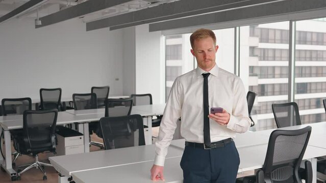 Busy professional business man standing in office holding mobile cellphone. Young businessman entrepreneur using smartphone cell phone technology device looking away at work.