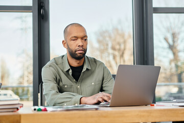 A man with myasthenia gravis sitting at a desk, focused on his laptop screen, working on a project...