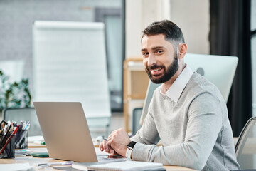 A man immersed in his work, sitting in front of a laptop computer in a modern office setting.