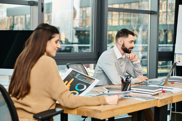 A man and woman engrossed in their laptops, collaborating on a project in a modern office setting.
