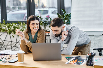 A man and woman in a corporate office focus intently on their laptop screen, working together on a project.