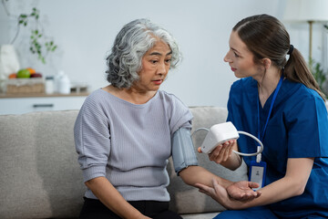 Female doctor checking old woman blood pressure at clinic and filling patient history in the...