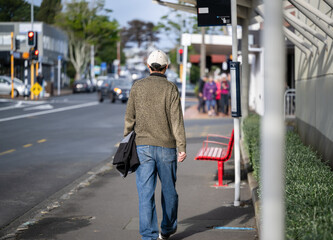Man walking to the bus stop on a busy suburban street. Unrecognizable people walking on the pedestrian sidewalk. Auckland.