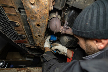 A mechanic wearing gloves under a car changes the oil filter in the garage. A mechanic installs a new oil filter under a car in the garage. Car repair in the garage.