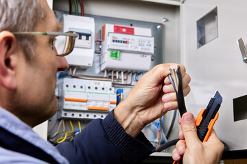 Cutting over sheath of power cable using retractable utility knife, electrician cuts outer sheath...