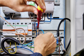 Electrician connects blue wire of power cable to neutral terminal bar in electrical panel during electrical installation work.