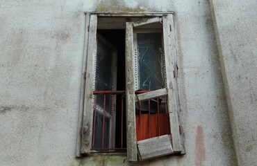 An open window with cracked frames and broken glass in an old abandoned house