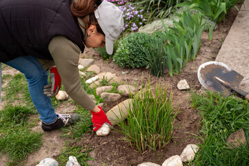 Woman laying out decorative stones on a flowerbed in the garden, country life concept
