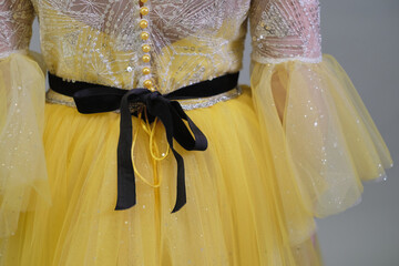 Close-up of a child s yellow princess dress with pearl buttons and a velvet ribbon, showcasing intricate design details.