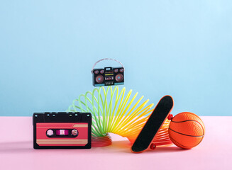 Creative still life with spiral spring rainbow toy, skateboard, cassette , boombox and baskeball ball on blue and pink. Back to 90s concept.
