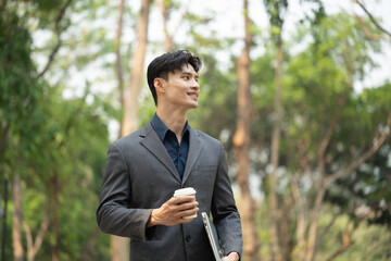 Professional businessman with takeaway coffee cup standing in the public park and looking away