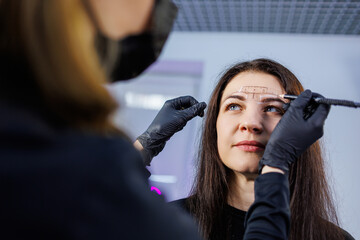A permanent makeup artist marks a woman's eyebrows with a pencil. Cometological procedure of...