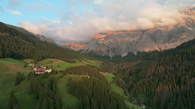 An evening aerial footage of secluded houses of the village of La Val with majestic Sas dles Nü (Cima Nove) mountain covered in beautiful clouds in the background. South Tyrol, Italy. LuPa Creative