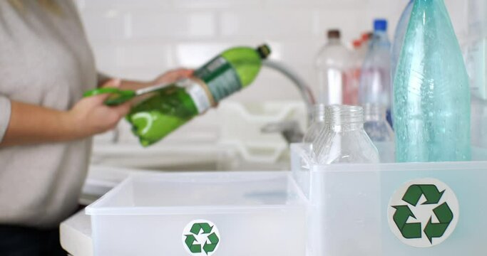 While sorting plastic for recycling in the kitchen, a woman cuts off labels from bottles. A woman at home in the kitchen puts plastic waste into different boxes to send them for recycling.