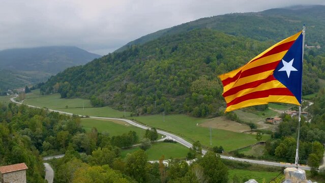 Panoramic view of a valley with a flag in close-up.
A valley in the Pyrenees of Catalonia, Spain, with the independence flag of Catalonia, moved by the wind on a cloudy day.