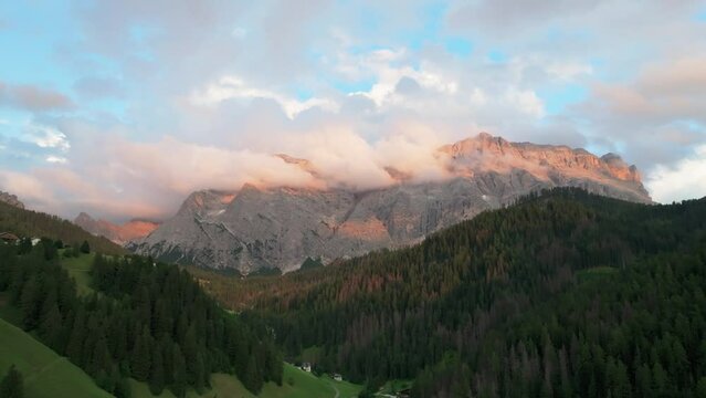 An evening aerial footage of the Sas dles Nü (Cima Nove) mountain covered in beautiful clouds. The drone is flying sideways above the valley in La Val village. South Tyrol, Italy. LuPa Creative.