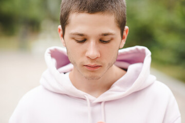 Handsome blond teenage boy 18-20 year old wearing hoodie looking down close up.