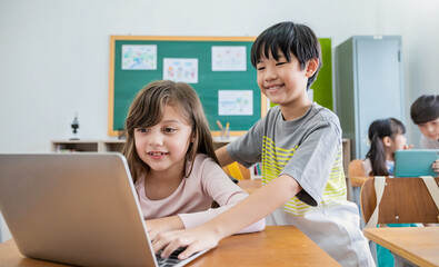 Portrait of Asian boy caucasian  girl use computer to learn lessons in elementary school. Student boy studying in primary. Children gadgets classroom. Education knowledge, technology internet network.