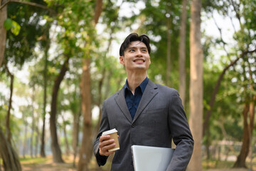 Fototapeta premium Professional businessman with takeaway coffee cup standing in the public park and looking away