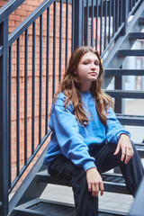 A student girl is sitting in beautiful clothes on an iron staircase. A photo shoot for a girl. - 789175362