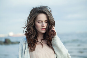 Pensive young woman model with brown hair and natural make-up walking along the shore of the resort...