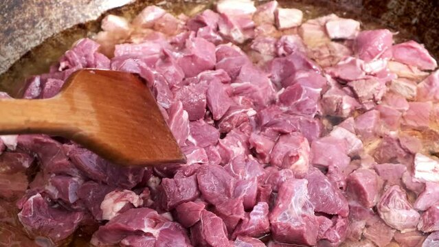 Frying lamb meat in a large cauldron in boiling oil to prepare national traditional pilaf in the open air using fire.