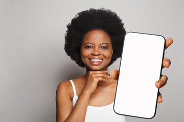 Portrait of healthy woman holding smartphone with white empty blank screen display on gray studio...