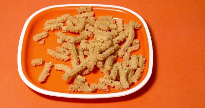 Close-up shot of hand taking butter murukku on plate against orange background. A popular snack of Tamil Nadu, India and prepared during festivals