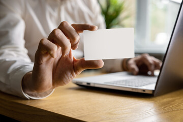 man showing blank business card while working on laptop in office. mockup