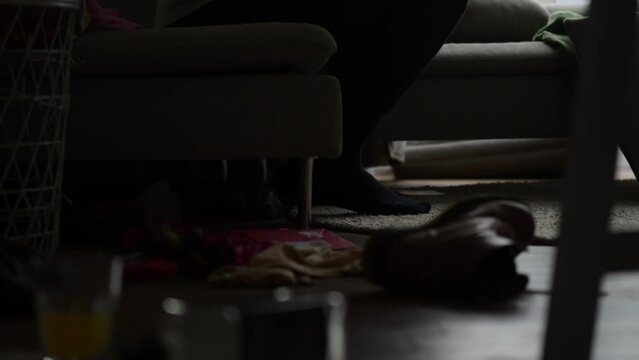A man overwhelmed by depression sits on a sofa, face hidden in hands, in a dark room with an empty bottle signaling alcoholism.