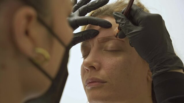 Beautician performing microblading on female client's eyebrows