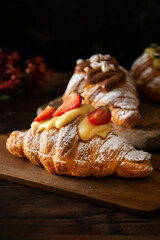 Freshly baked croissant, with strawberries and cream on top. Dark wooden background