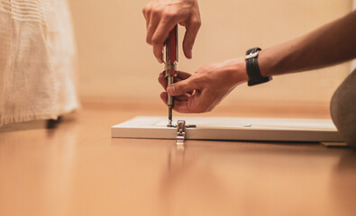 The hands of a young man are twisting a screw with a screwdriver.
