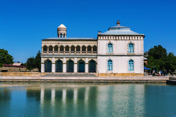 Emir's Summer Palace in Bukhara reflected in pond, clear sky, exemplifying Uzbek architecture....