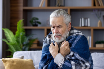 A close-up photo of a gray-haired older man sick from the virus, who is sitting at home on the sofa...