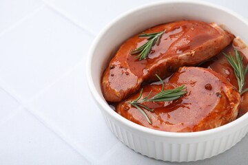 Raw marinated meat and rosemary in bowl on white tiled table, closeup. Space for text