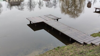 Wooden pier and pond surface with reflection of trees in rainy weather