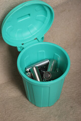 Used finger batteries in a miniature trash can. on a beige dirty background.
