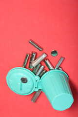 Used finger batteries in a miniature trash can. Pink background.