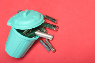Used finger batteries in a miniature trash can. Pink background. Field for text.