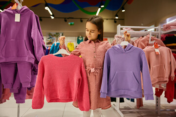 Little girl child choosing between sportive sweatshirt and traditional sweater - 789226385