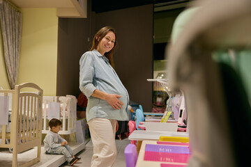 Happy pregnant mother doing shopping choosing safety furniture for newborn - 789226705